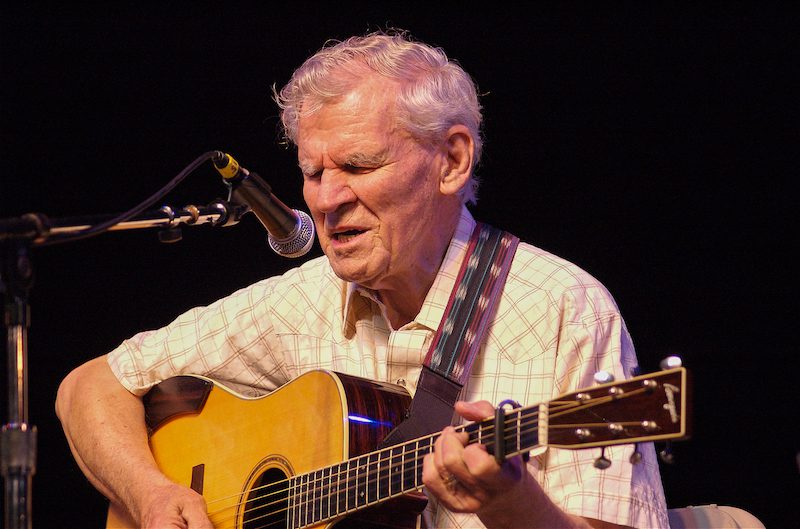 Doc Watson playing acoustic guitar and singing onstage