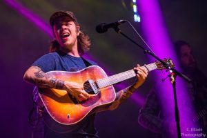 Billy Strings plays guitar onstage with purple spotlights in the background