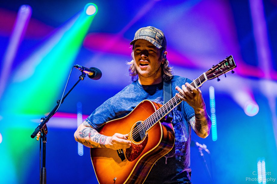 Billy Strings onstage with guitar backed by colorful lights