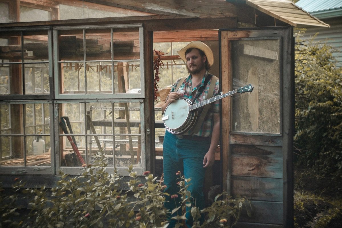 Willi Carlisle stands in a doorway with a banjo