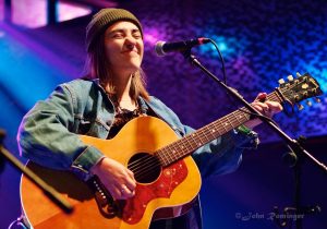 Margo Cilker closes her eyes while playing an acoustic guitar onstage