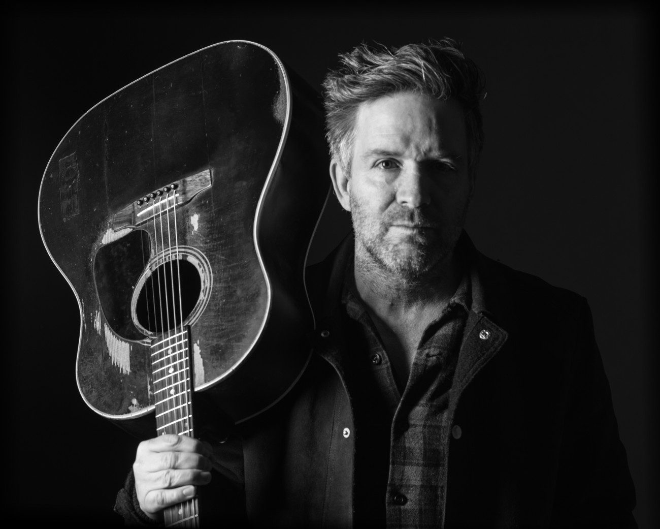 A black and white portrait of Tim Easton holding a guitar