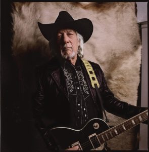 A color photos of John Anderson and a dark electric guitar with yellow strap