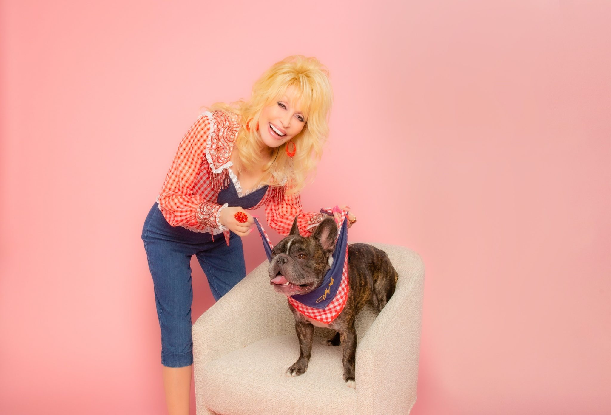 Dolly Parton with a French bulldog on a pink backdrop