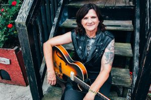 Amy Ray with guitar sitting on a set of grimy metal stairs
