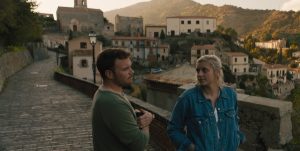 A still of the male and female lead actors from A Chance Encounter against an Italian village scape