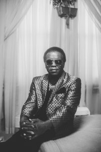 Black and white portrait of Lee Fields sitting in a pattern jacket