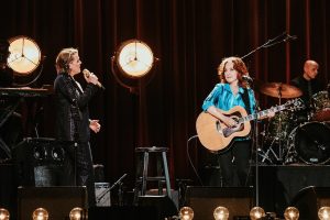 Brandi Carlile and Bonnie Raitt look at each other while singing onstage
