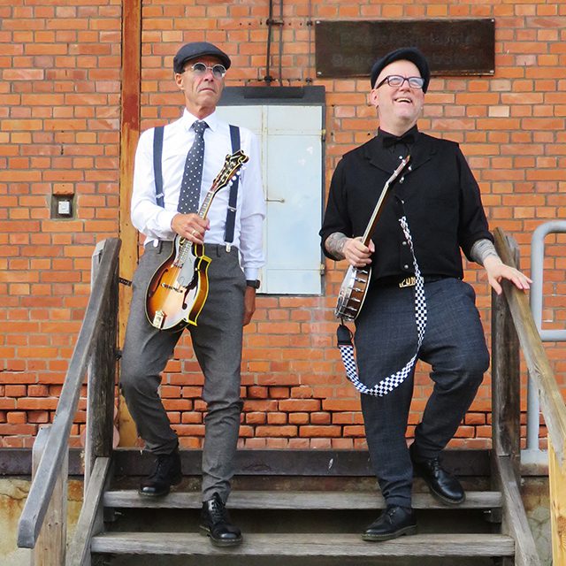 The duo Ukes of Tomorrow in front of a brick wall