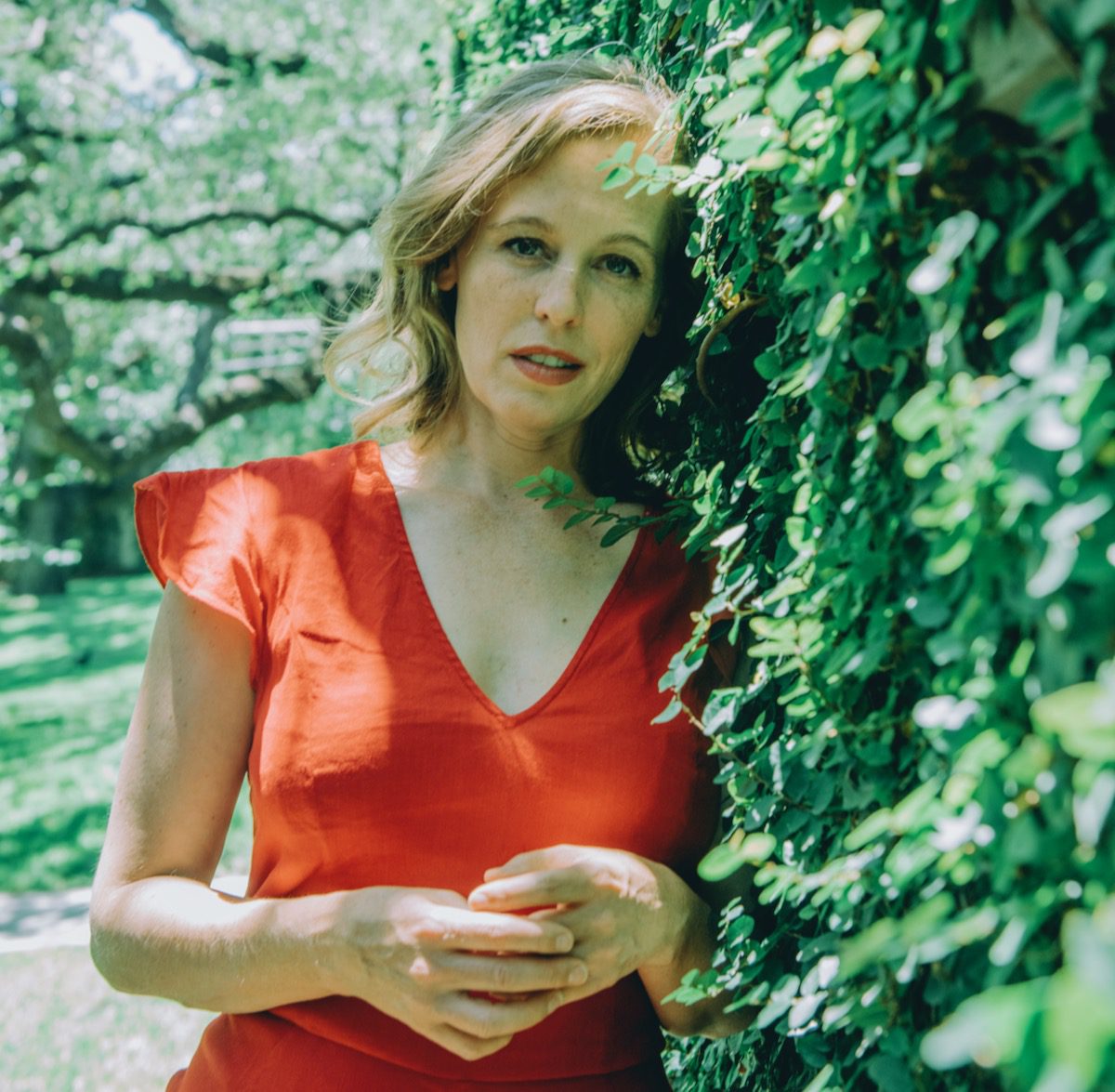 Tift Merritt in red dress leans against an ivy wall