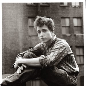 A black and white portrait of a young Bob Dylan seated