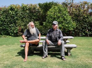 Neil Young and Rick Rubin sit at a picnic table on a sunny day