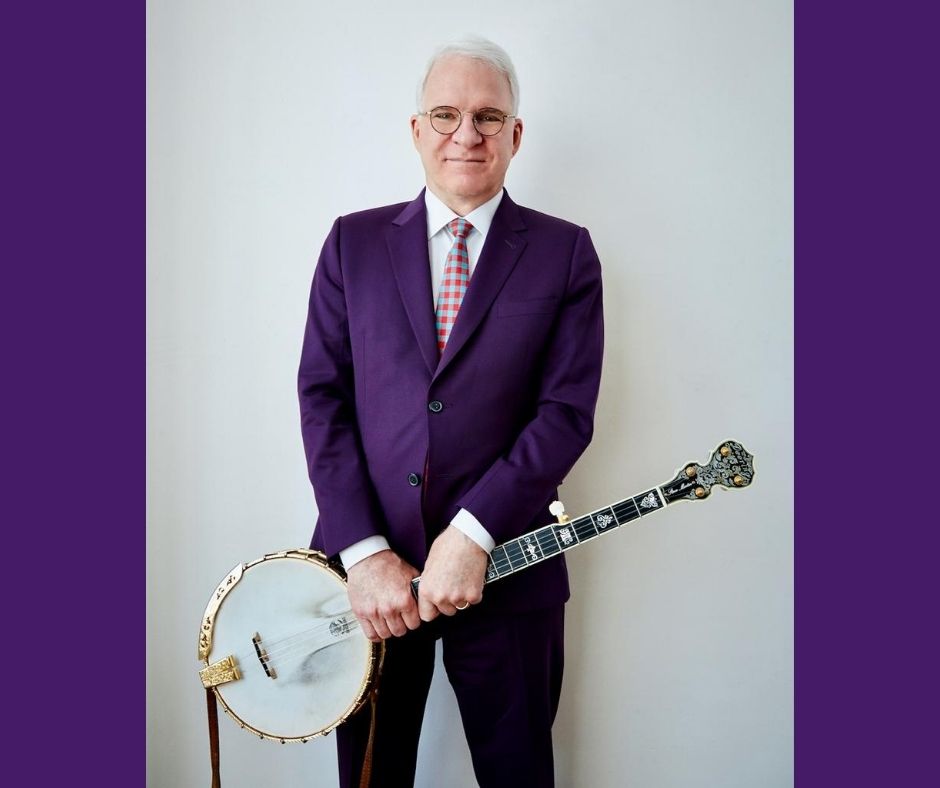 Steve Martin in a purple suit holds his banjo