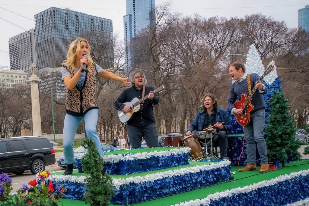 Nikki Glaser on a parade float in Chicago dressed like Ferris Bueller, backed by Wilco on instruments