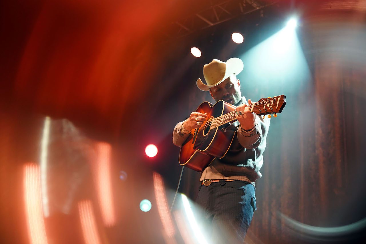 Charley Crockett onstage with red and white lights blurred in the background