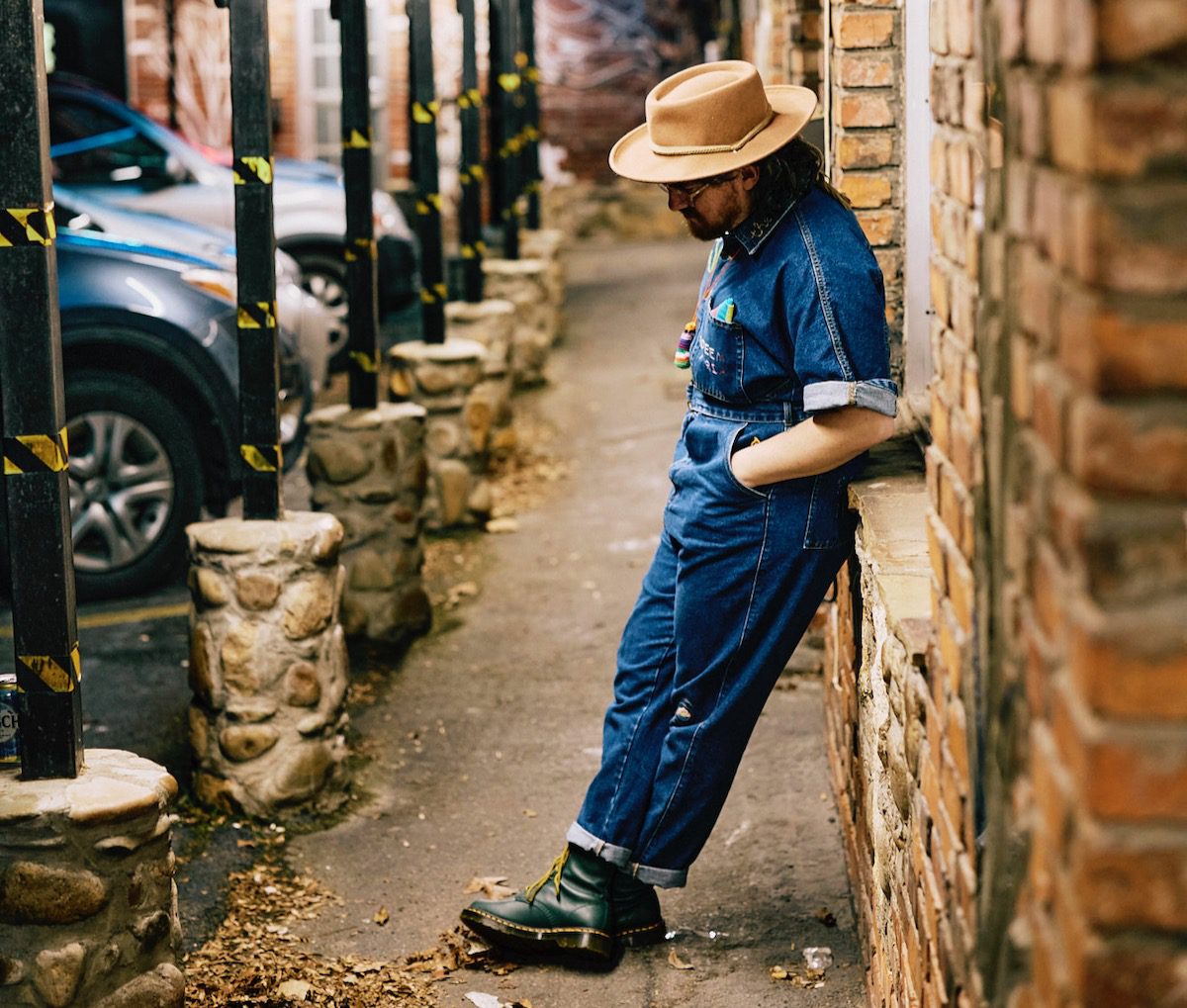 Adeem the Artist leans against the brick wall of a business.