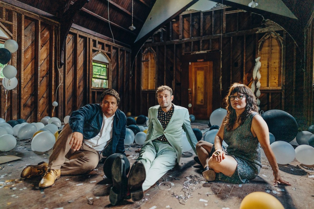 Nickel Creek's Sean Watkins, Chris Thile, and Sara Watkins in a decaying building filled with balloons.