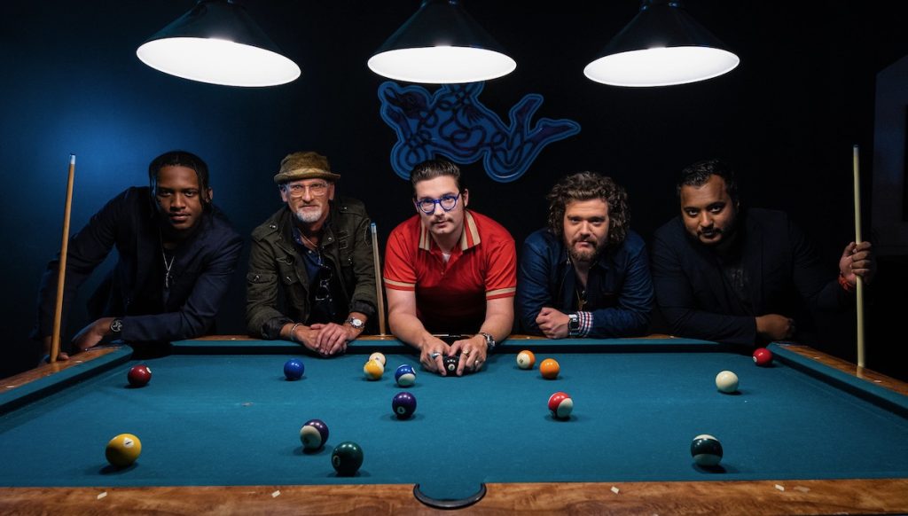 Eddie 9V and band lean on a pool table in a dark room