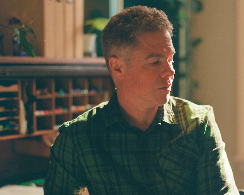 Josh Ritter in a sunlit room seated by a desk with cubbies filled with markers.