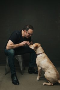 Mark Erelli, seated, bends to smile at his yellow lab, Leo