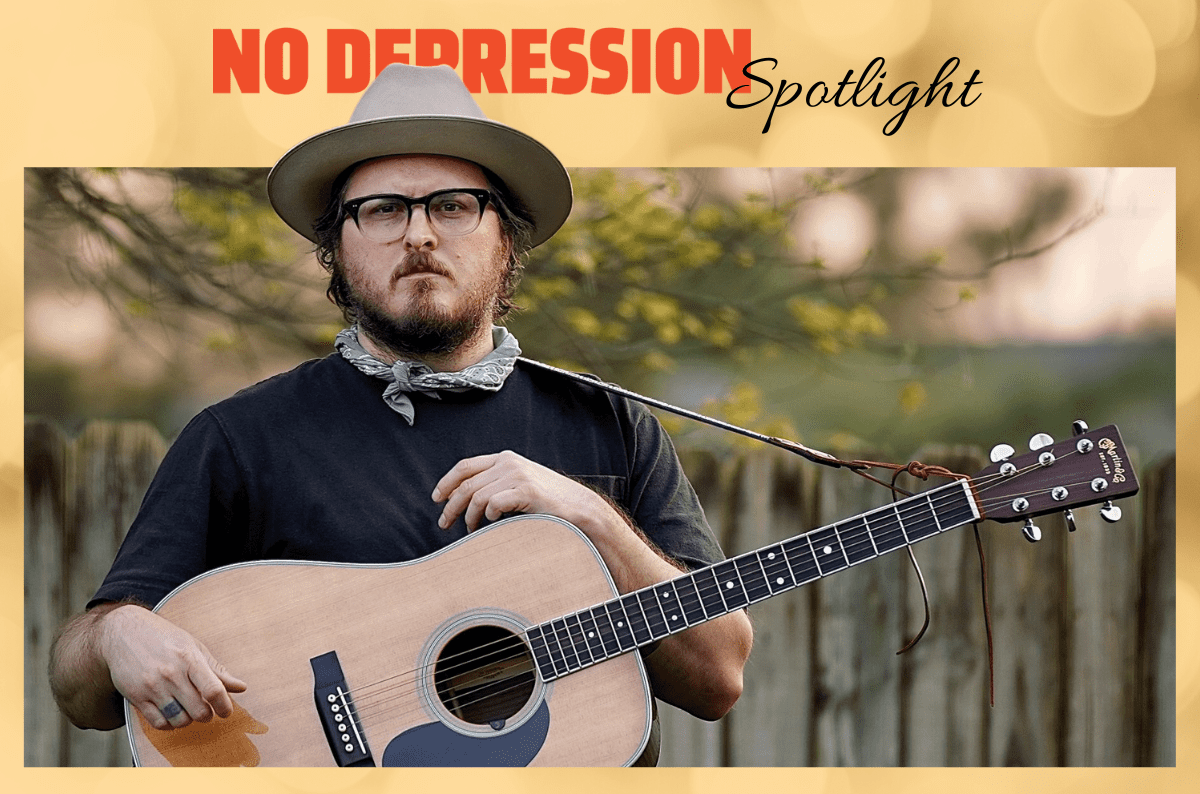 Pony Bradshaw stands in front of a wooden fence with acoustic guitar.