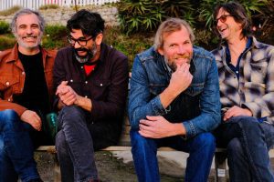 The four members of The Mother Hips sitting on a stone wall