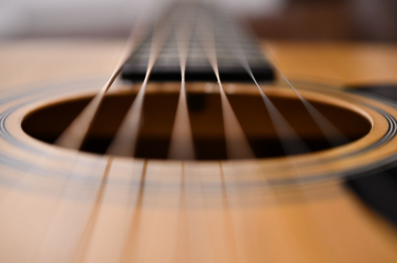 Looking down six guitar strings toward the acoustic instrument's fretboard