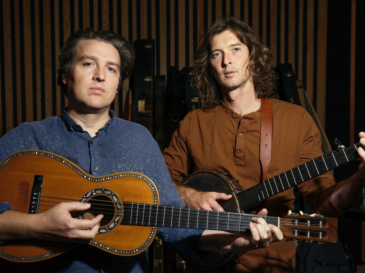 The Milk Carton Kids hold acoustic instruments in a somber portrait