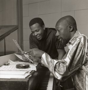 Isaac Hayes and David Porter look at a piece of sheet music at a piano in a black and white image