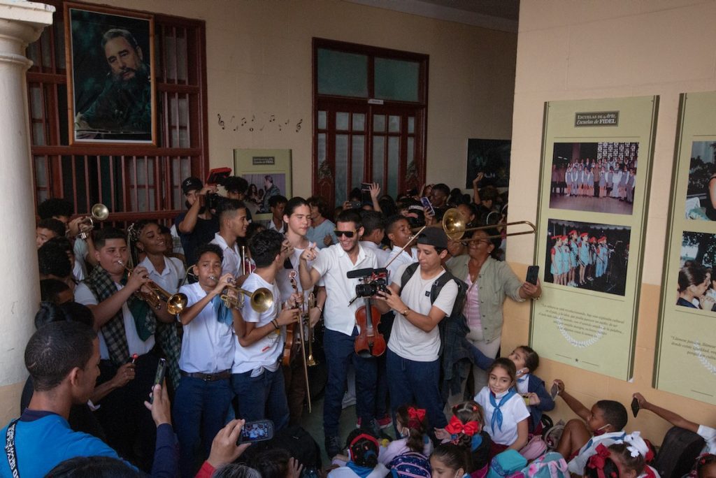 Students with instruments jam into a small space under a photo of Fidel Castro
