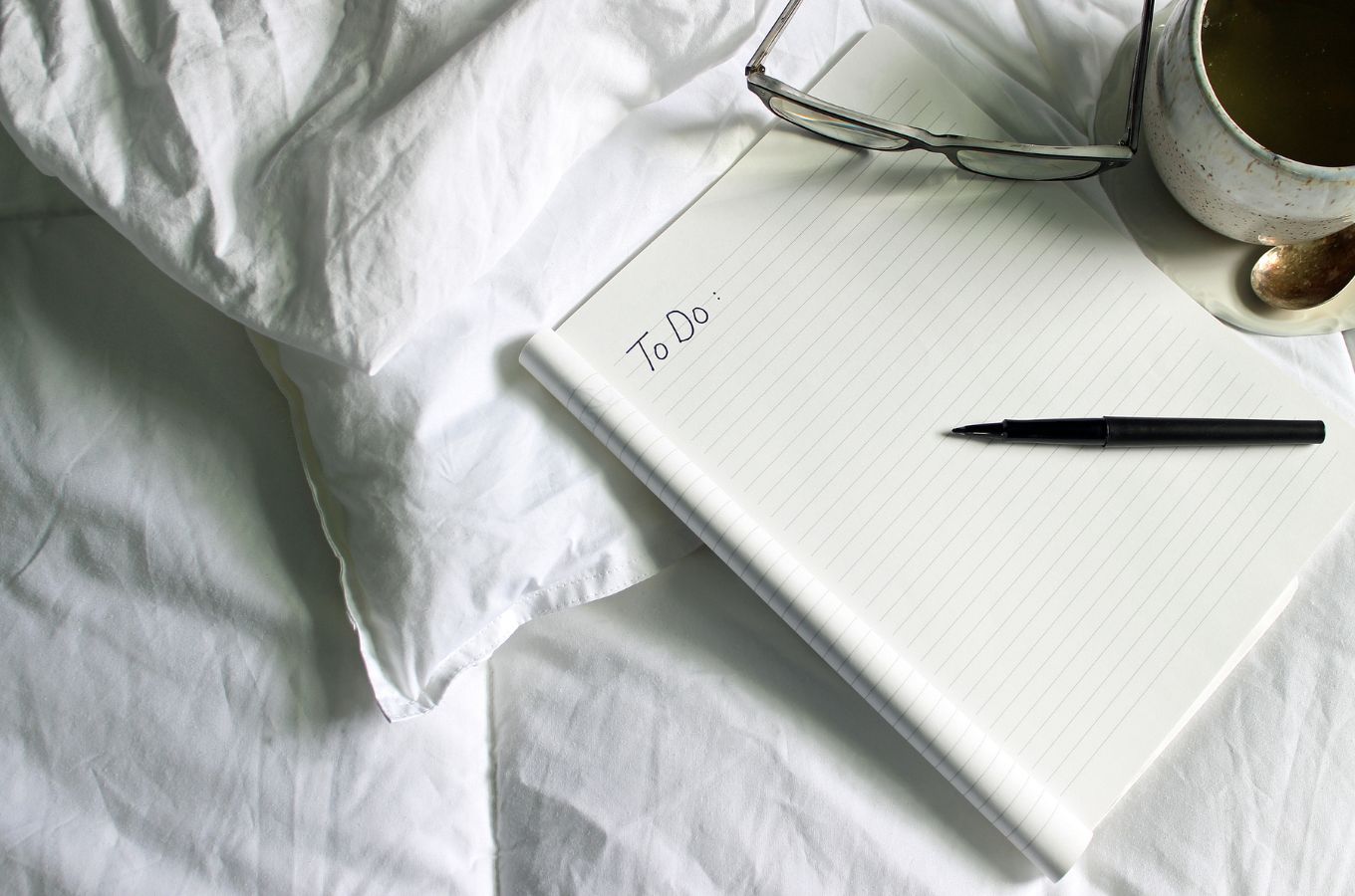 A notebook with "to-do" written on the top page on a white duvet cover