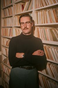 Nick Waterhouse in black shirt leaning against shelves of records