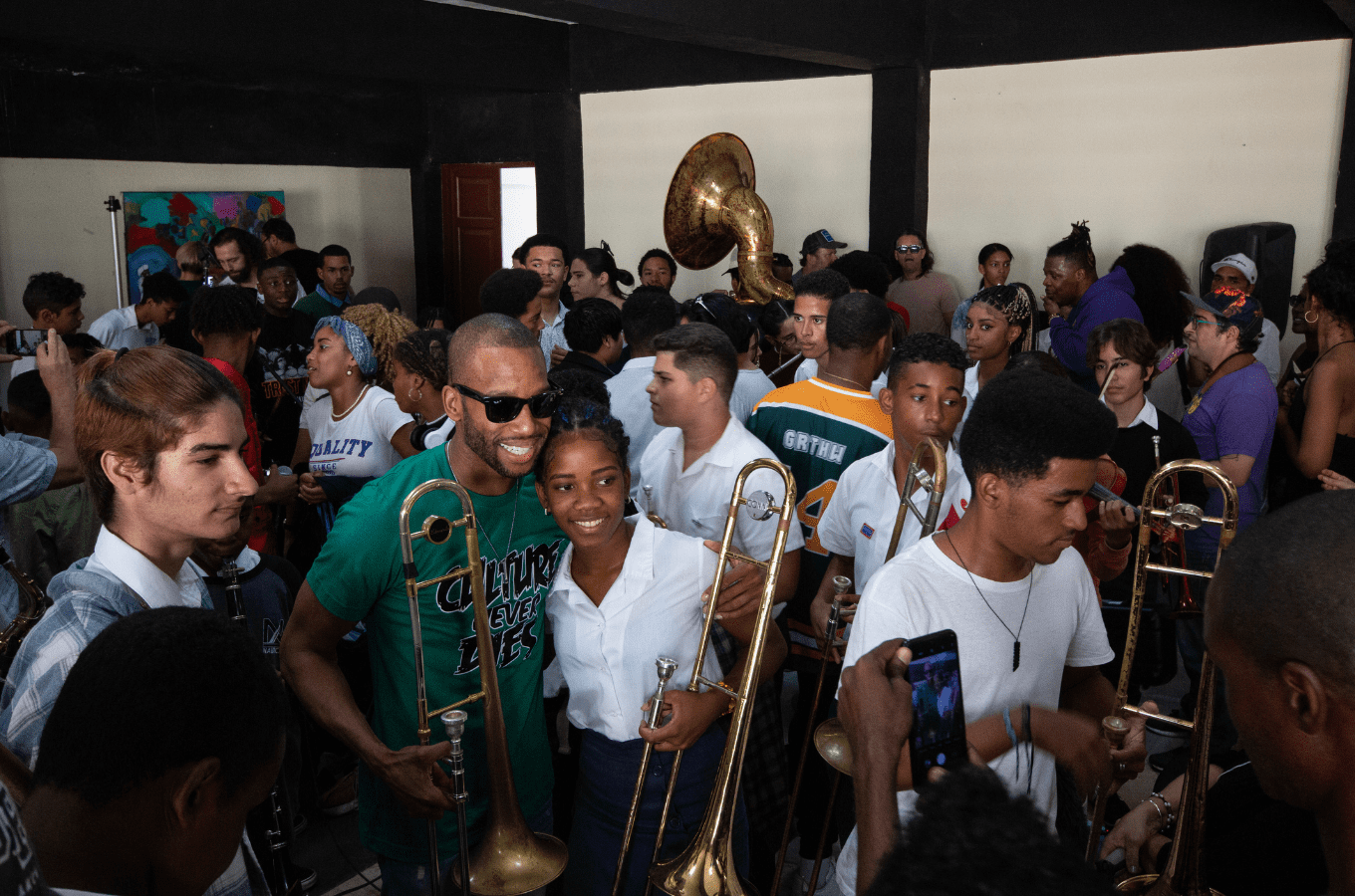 Trombone Shorty poses for a photo in a room full of students with brass instruments