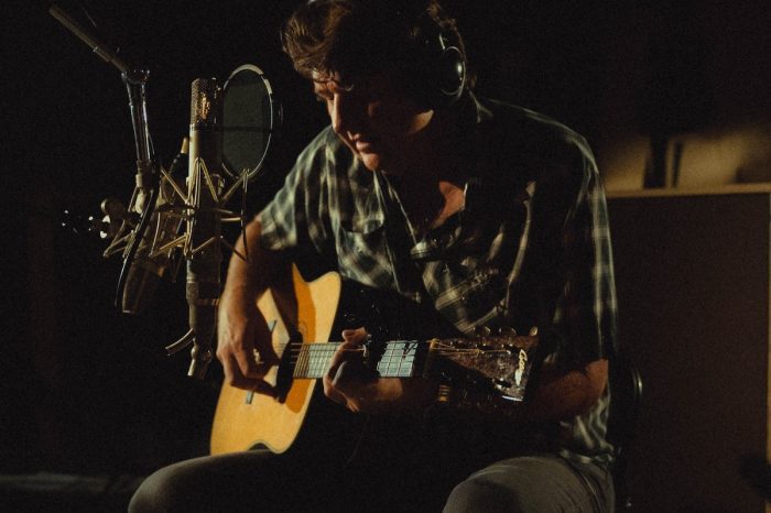 Bruce Robison playing acoustic guitar in a dark studio