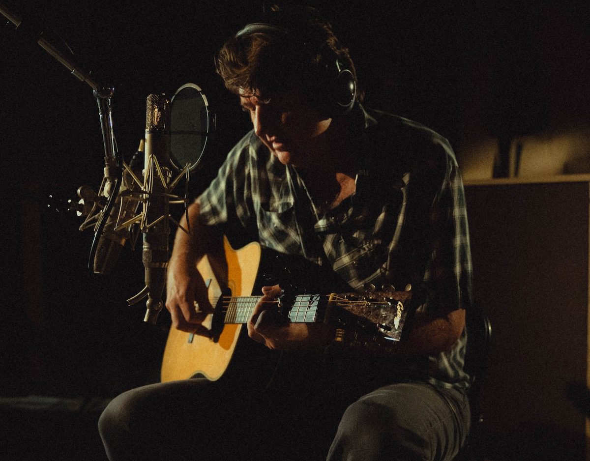 Bruce Robison playing acoustic guitar in a dark studio