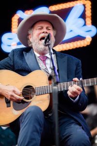 Robert Earl Keen, seated, plays an acoustic guitar on stage