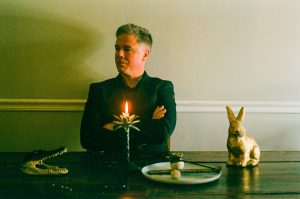 Josh Ritter sits at a table with a round tray, rabbit figurine, and other knickknacks.