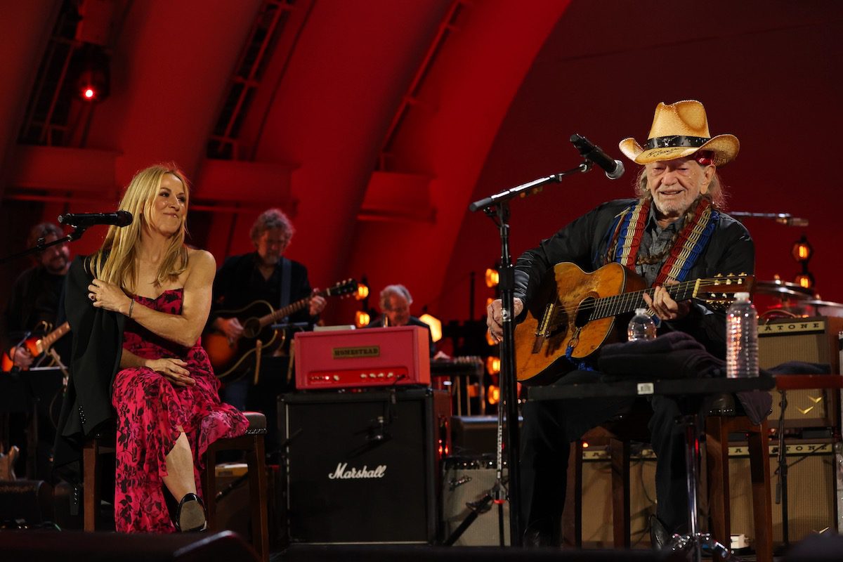 Sheryl Crow and Willie Nelson on stage with a red background