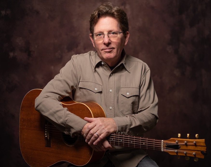 Tim O'Brien sits with acoustic guitar