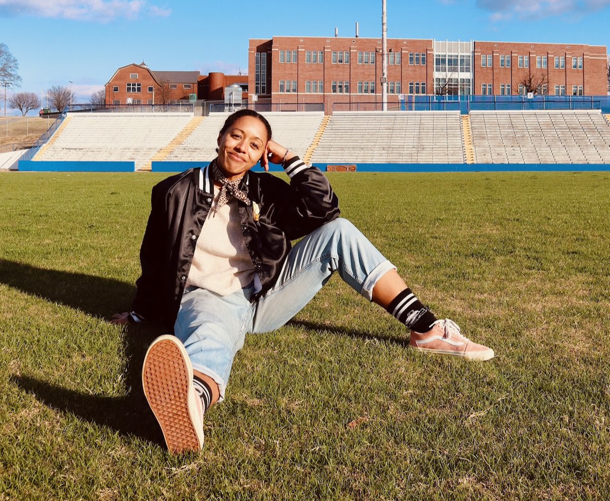 Lizzie No sitting on a grassy athletic field with bleachers in the background