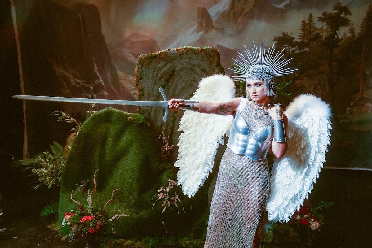 Sierra Ferrell wears white wings and silver armor and points a sword