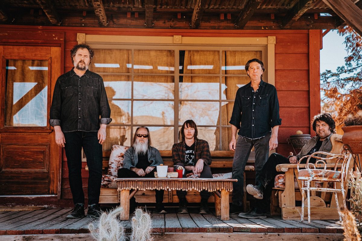 The five members of Drive-By Truckers on a wooden cabin porch with a cactus in the foreground