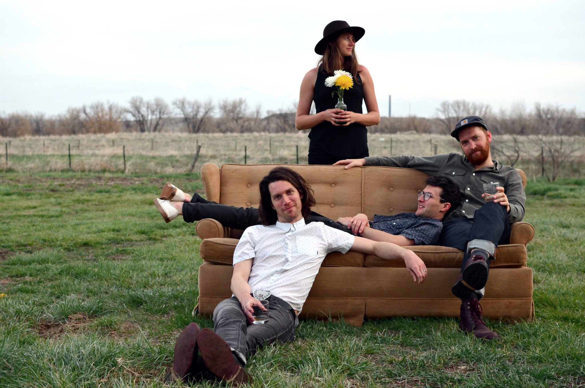 Portrait of the four band members arranged on a couch in a field